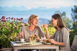 Zwei Frauen sitzen draußen im Cafe und genießen eine Torte
